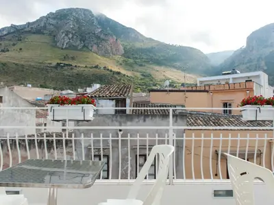 a balcony with a table and chairs and mountains at White in Castellammare del Golfo