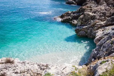 a beach with blue water and a rocky shore at Casa Turano in Castellammare del Golfo