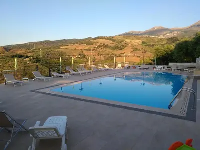 a large swimming pool with chairs and mountains in the background at Agriturismo le Campanelle - Sicilia - Cefalù in Lascari