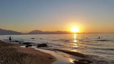 a sunset on the beach with people in the water at Villa sul mare Palazzolo in Trappeto