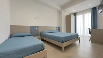 a bedroom with two beds with blue sheets and a window at B&B Vista Mare in San Vito lo Capo