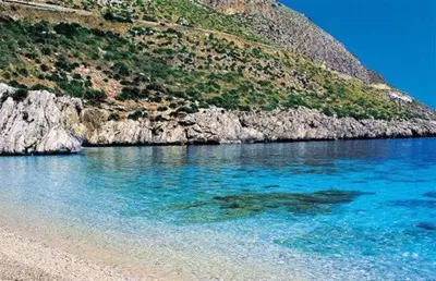 a beach with blue water next to a mountain at Grace's Place in Scopello