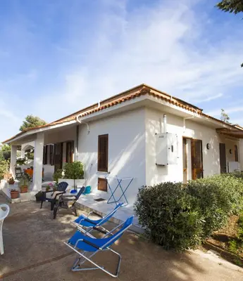 a white house with blue chairs in front of it at Grace's Place in Scopello