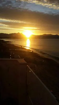 a sunset on a beach with the sun setting over the ocean at Villa Mare Ficarazzi in Ficarazzi