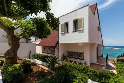 a house with a tree next to the ocean at Vero Sicily - Villa San Giorgio in Cinisi