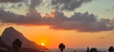 a sunset with a mountain and palm trees in the foreground at Al Civico 365 in Castelluzzo