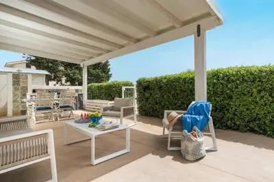 a patio with white chairs and a table and awning at Spuma di Mare - Riccio in San Vito lo Capo