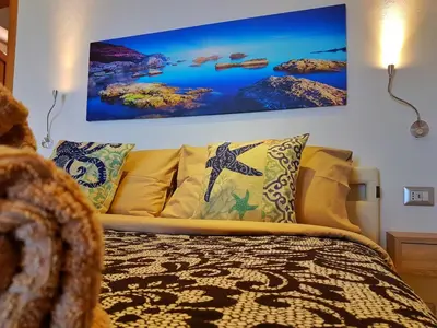 a bed with yellow pillows and a painting on the wall at Brezza Marina Guesthouse in Cefalù