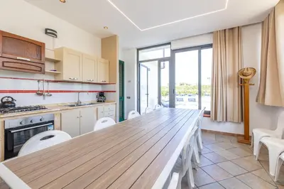 a kitchen with a long wooden table and white chairs at Villa Arvilla with Private POOL in Campofelice di Roccella