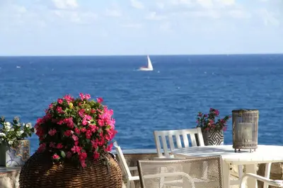 a table with a basket of flowers and a boat in the ocean at Villa Majus in Porticello