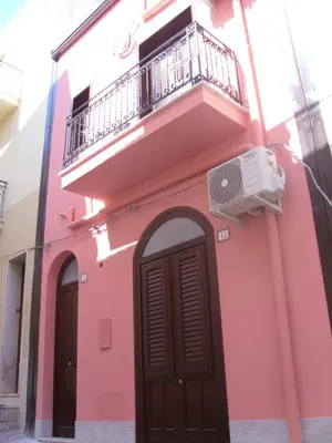 a pink building with a balcony and a door at Casa di Cecilia in Castellammare del Golfo