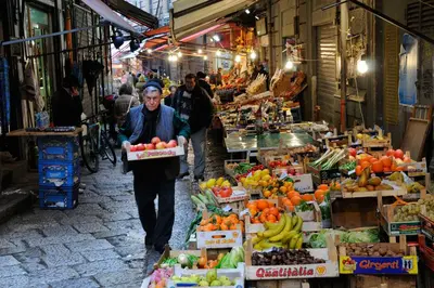 a man walking through a market with boxes of fruits and vegetables at Casa Samu in Palermo