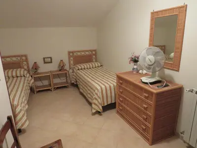 a bedroom with two beds and a fan on a dresser at Villa Rosada in Castellammare del Golfo