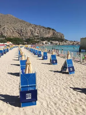 a row of blue beach chairs on a sandy beach at Ashur apartments in Mondello