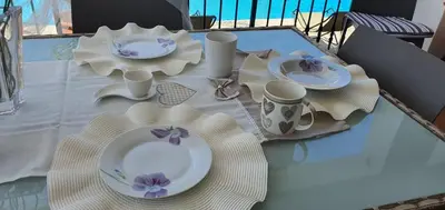 a table with white plates and purple flowers on it at 25min da Cefalù e Palermo Piscina pvt, 4camere, 150m dal mare in Trabia