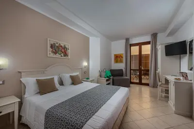 a bedroom with a large bed and a living room at Helios Hotel in San Vito lo Capo