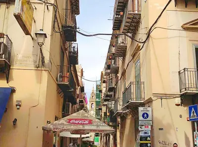 a narrow street with buildings and shops in a city at Orologio del Massimo in Palermo