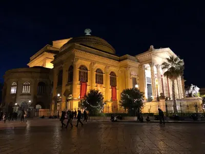a large building with people walking in front of it at night at Orologio del Massimo in Palermo