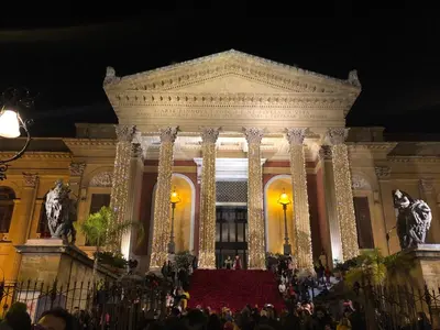 a large building with people in front of it at night at Orologio del Massimo in Palermo