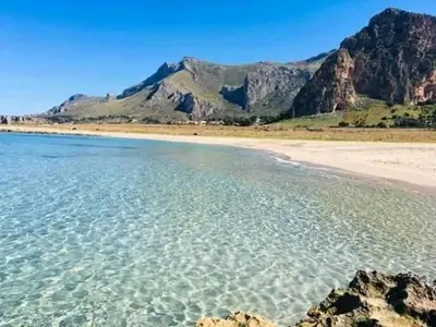 a beach with clear water and mountains in the background at Le Case di Palma - Viola in San Vito lo Capo