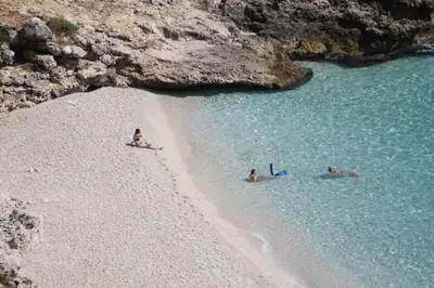 three people are swimming in the water on a beach at Le Case di Palma - Viola in San Vito lo Capo
