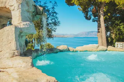 a swimming pool with a waterfall and a body of water at CDSHotels Terrasini - Città del Mare in Terrasini