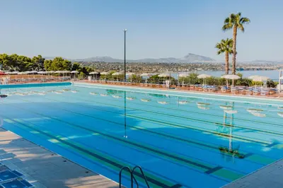 a large swimming pool with palm trees and a body of water at CDSHotels Terrasini - Città del Mare in Terrasini
