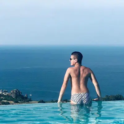 a man in a swimming pool looking out at the ocean at Hotel Antica Cascina Del Golfo in Scopello