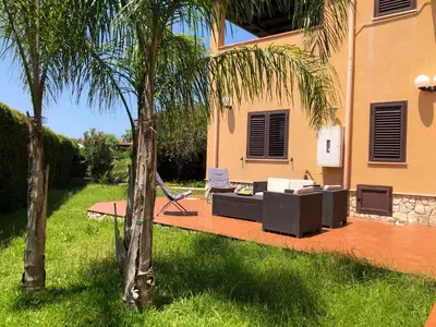 a patio with a couch and a chair and palm trees at Villa Aga in Campofelice di Roccella