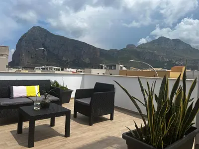 a balcony with chairs and tables and a mountain at sicily home casa vacanze con piscina in San Vito lo Capo
