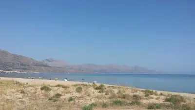 a beach with people standing on the sand and water at Elios casevacanze sulla spiaggia in Alcamo