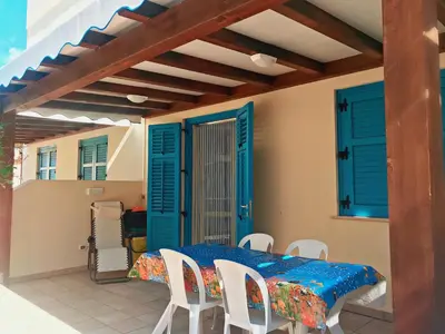 a patio with a table and chairs and blue shutters at appartamento residence via giardini Acquamarina in San Vito lo Capo