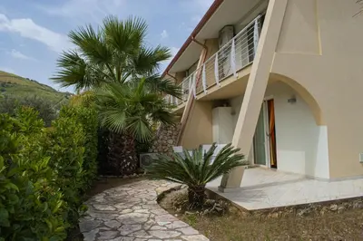 a house with a palm tree next to a walkway at Borgo Aranci - Villetta a Schiera A1 in Castellammare del Golfo