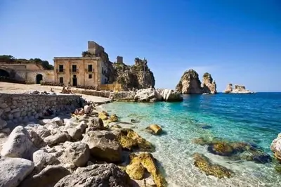 a beach with rocks and a building in the water at Il Sole di Sicilia in Castellammare del Golfo