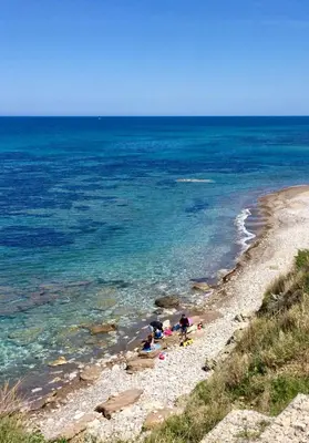 a group of people on a rocky beach near the ocean at Sfondo Blu Villa sul mare in Trabia
