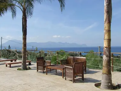 a group of benches and palm trees with the ocean in the background at Petruso Resort e SPA in Balestrate