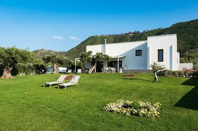 a house with a lawn with two chairs in the yard at Nettuno in Cefalù