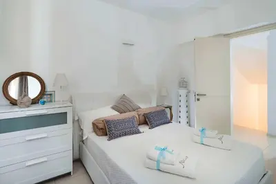 a white bedroom with a bed and a mirror at Nettuno in Cefalù