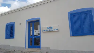 a white building with blue doors and a sign on it at L'isola del sole in Castelluzzo