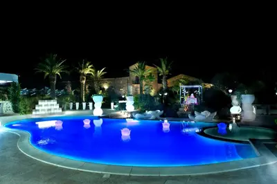 a large blue swimming pool at night with palm trees at Borgo degli Angeli Wellness & Resort by Le Dhome Sicily in Balestrate