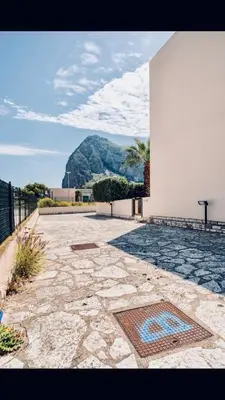 a stone walkway with a building and a mountain in the background at Appartamento BluOltreMare in San Vito lo Capo