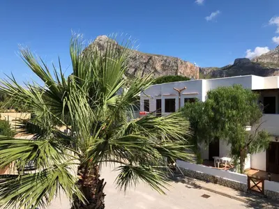 a palm tree in front of a building with a mountain at Residence Smeraldo in San Vito lo Capo