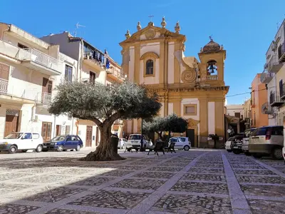a tree in front of a building with a clock tower at Mizzika Vacanze in Castellammare del Golfo