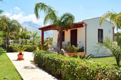 a white house with palm trees and a garden at Residence I Faraglioni in Scopello