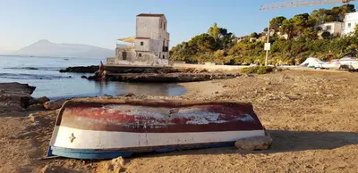 a boat sitting on the shore of a beach at La Caletta in Santa Flavia