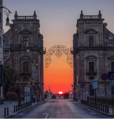 two buildings on a street with a sunset in the background at Hello Cathedral House in Palermo
