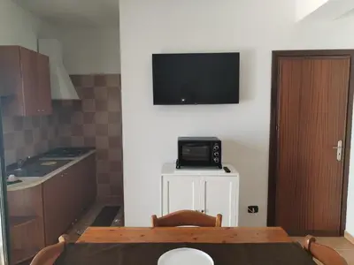 a kitchen with a table and a tv on a wall at Casavacanze corallo in Isola delle Femmine