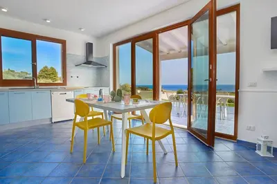 a kitchen with a table and chairs and the ocean at VILLA ANANDA in Scopello