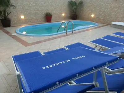 a pool with blue chairs in front of a swimming pool at Hotel Altamarea in San Vito lo Capo