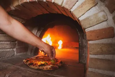a person putting a pizza into a brick oven at RESORT Valle del Re in Partinico